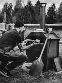 "En man lagar mat i Faster Greta, en vedeldad bak- och matlagningsugn."