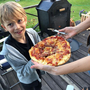 "En pojke serveras pizza gräddad i den vedeldade ugnen som syns i bakgrunden."